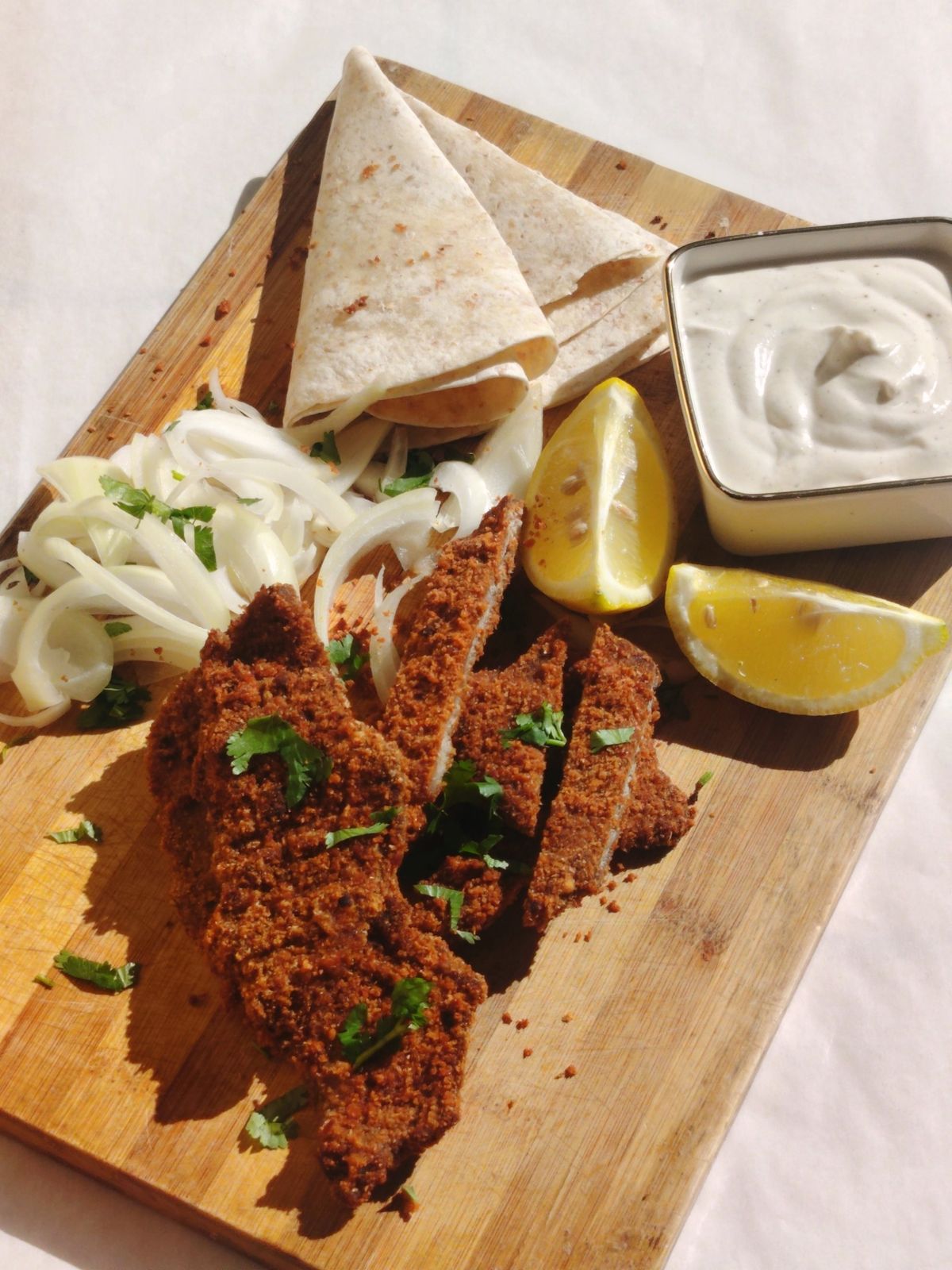 Aqashi with flatbread, sliced onion, lemon wedges and white sauce on a board