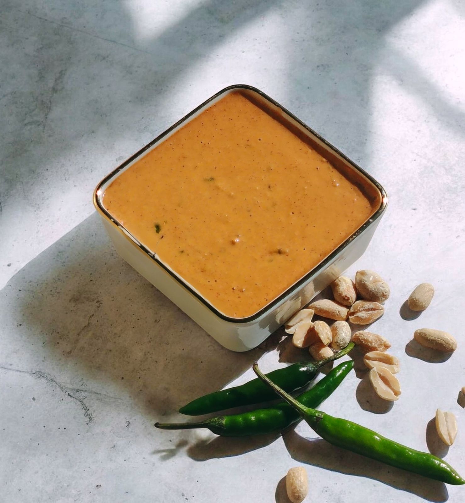 Peanut chilli sauce in a gold-rimmed bowl with roasted peanuts and green chillies