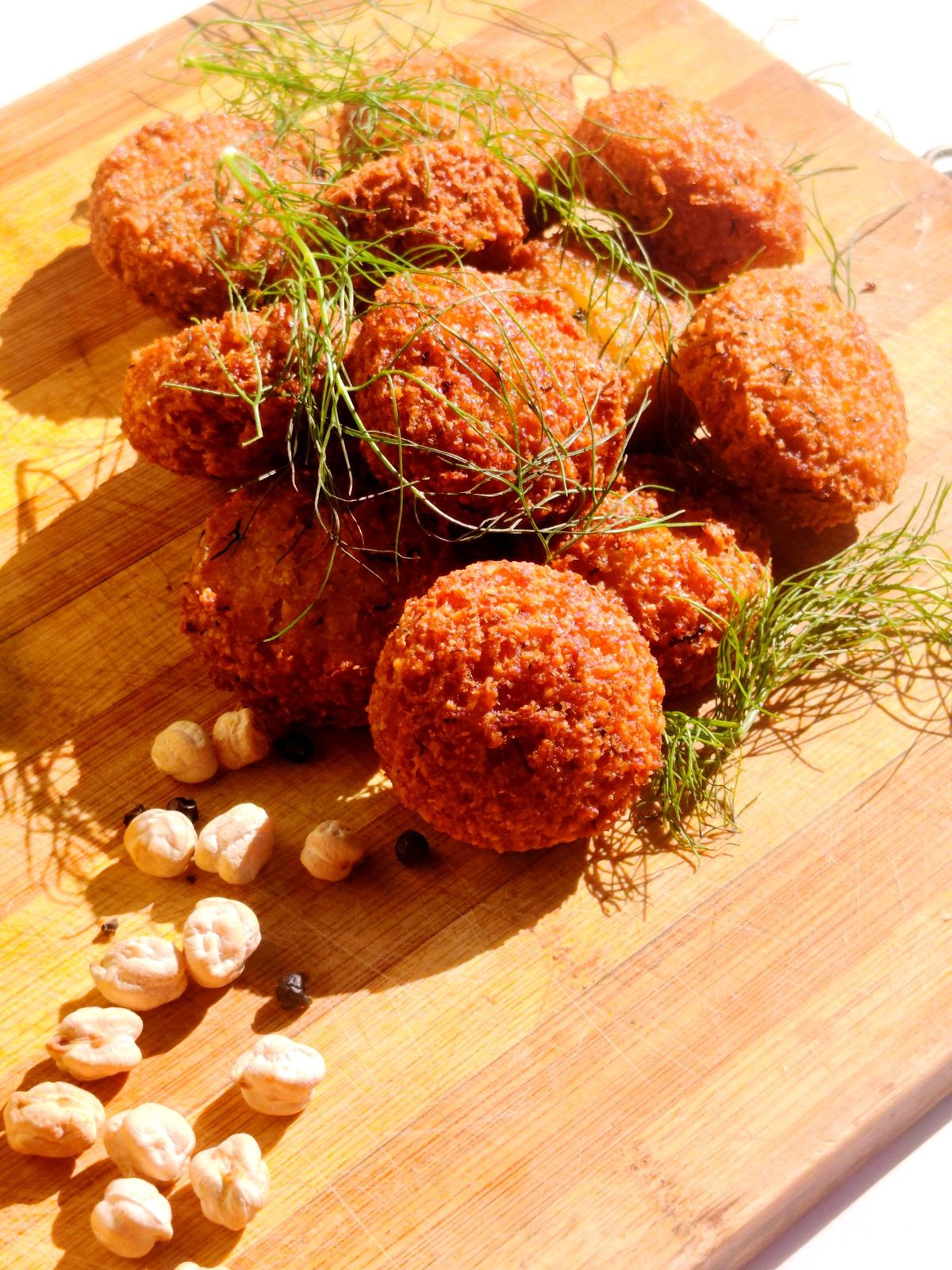 Freshly fried falafel with fennel fronds and dried chickpeas on a wooden board