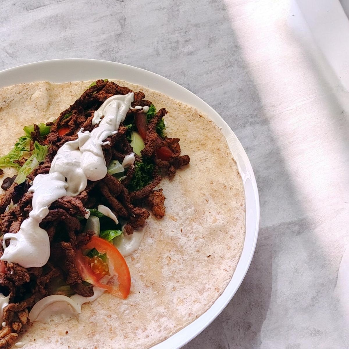 An open beef wrap with salad, tomato and white sauce on a plate