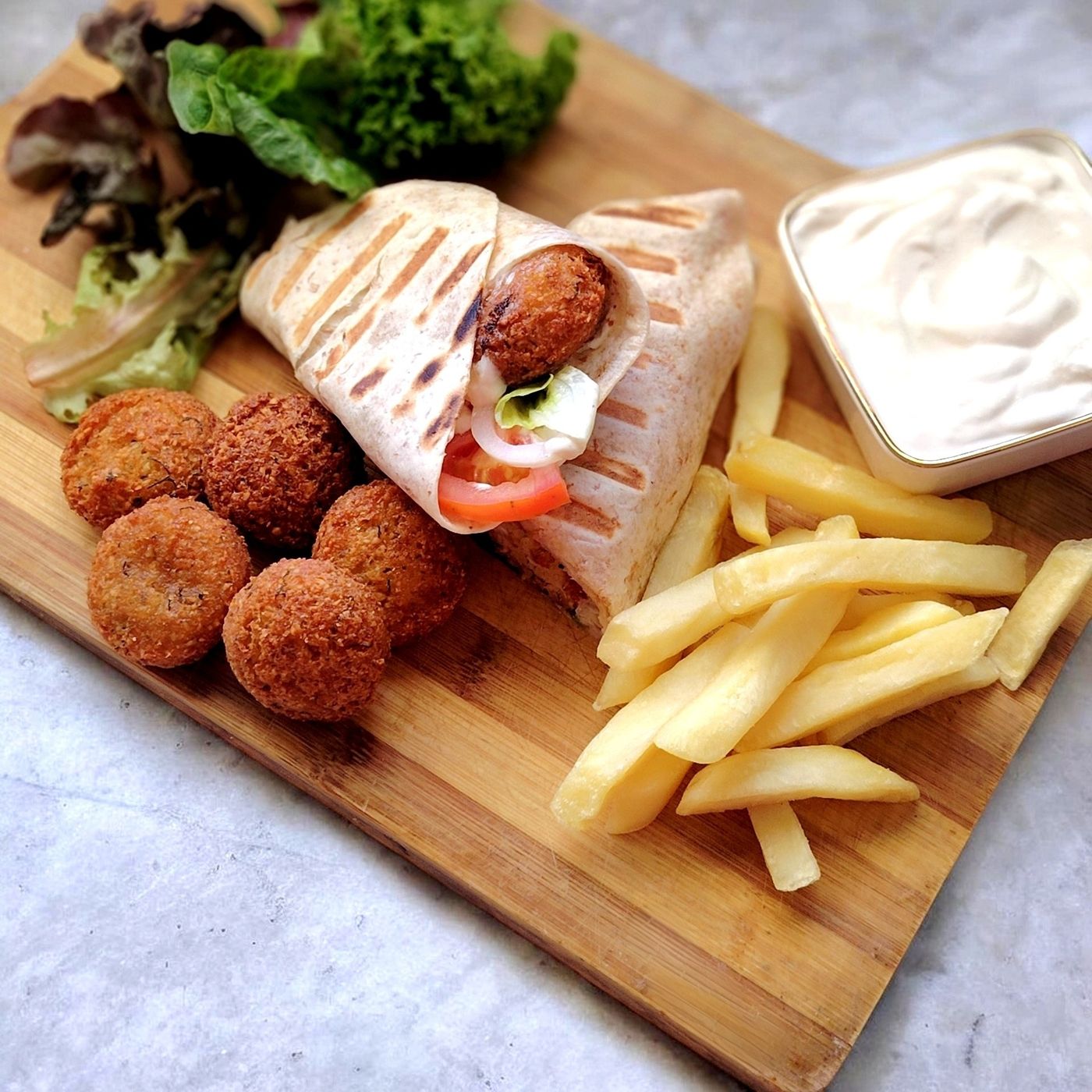 A grilled falafel wrap with loose falafel, chips, salad and white sauce