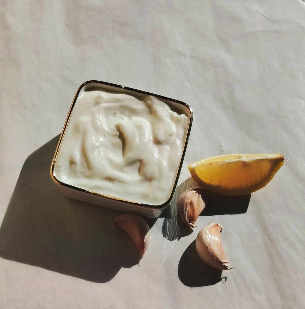 Garlic sauce with garlic cloves and a lemon wedge