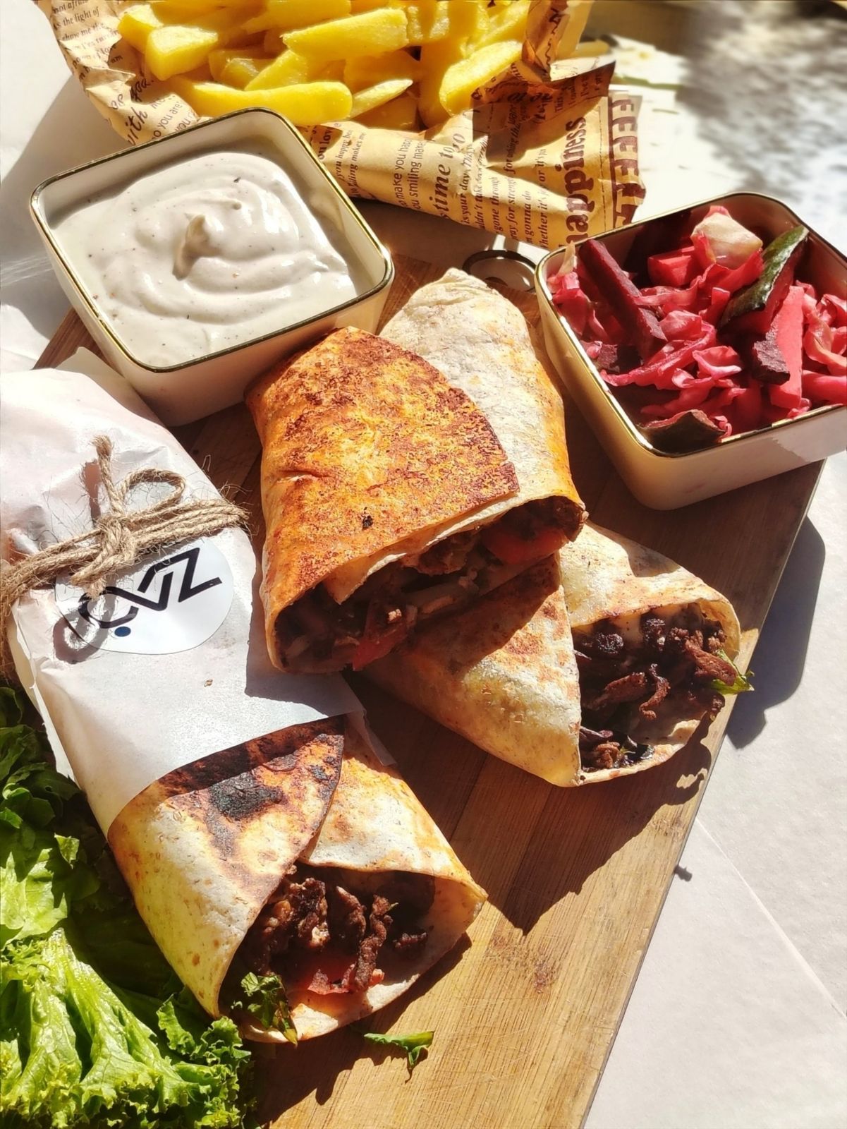 A board of beef wraps with chips, white sauce and pickled vegetables