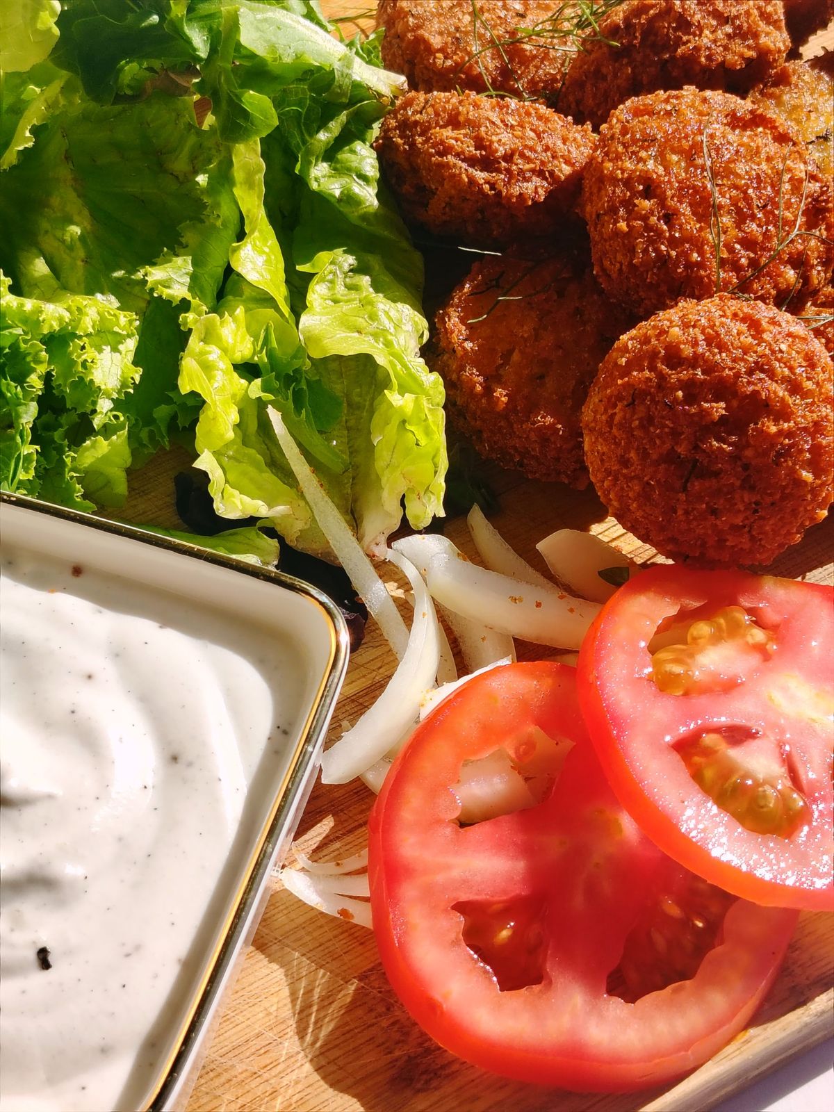 Falafel with lettuce, sliced onion, tomato and a bowl of white sauce in the sun