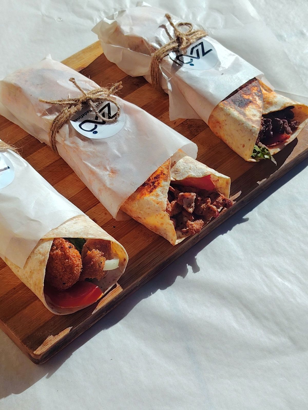 Falafel, chicken and beef wraps in Zad paper, tied with twine on a wooden board